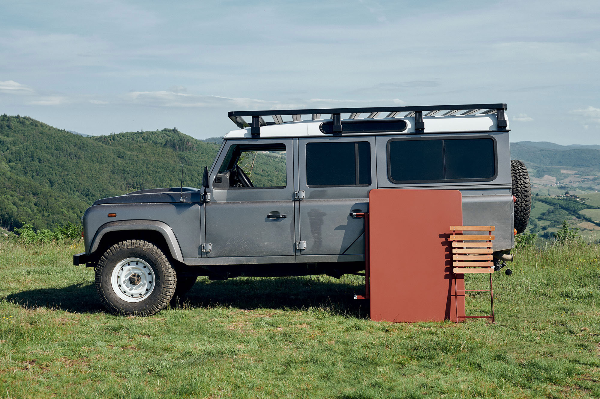 Der BISTRO_Stuhl naturel zusammengeklappt vor einem Landrover Defender