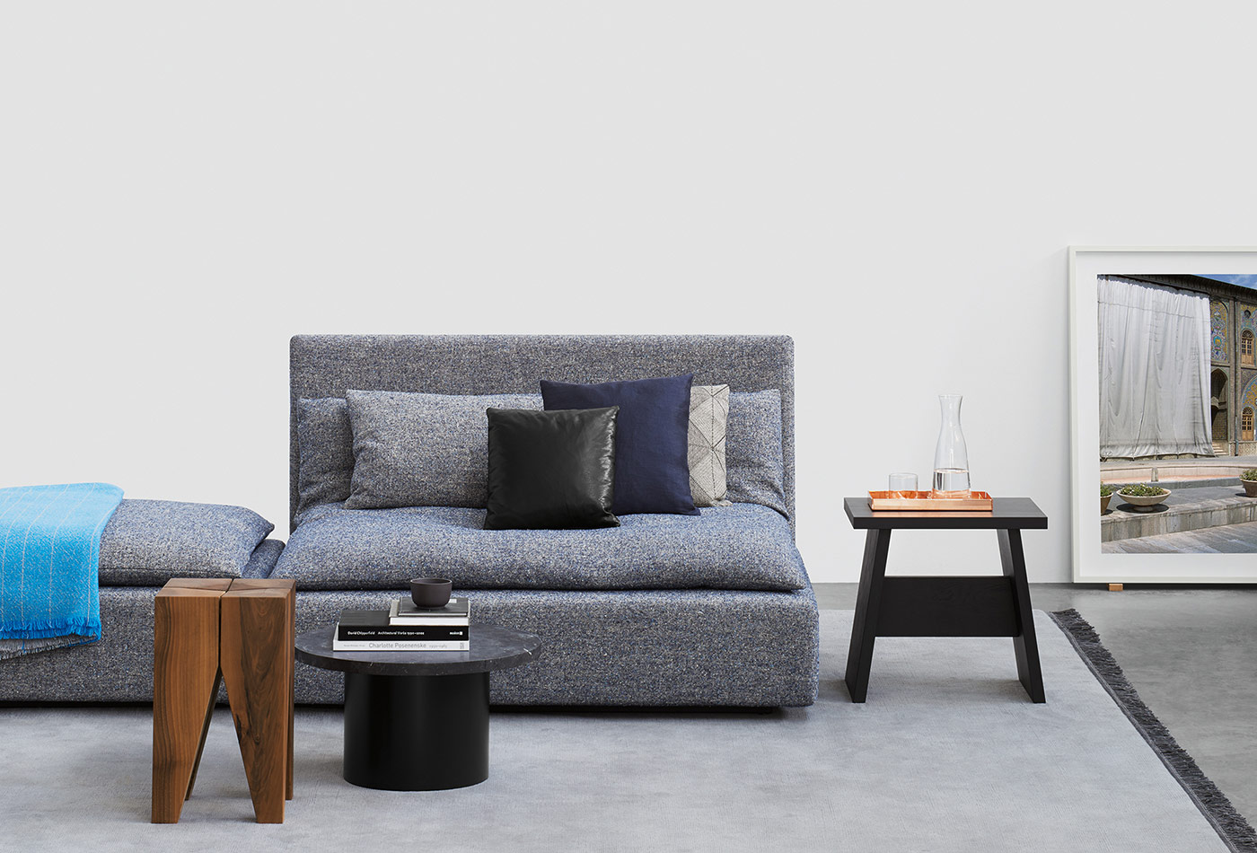 Das e15 Sofa Shiraz in blau, daneben der Hocker Langley in schwarz und der Hocker Backenzahn neben dem Beistelltisch Enoki